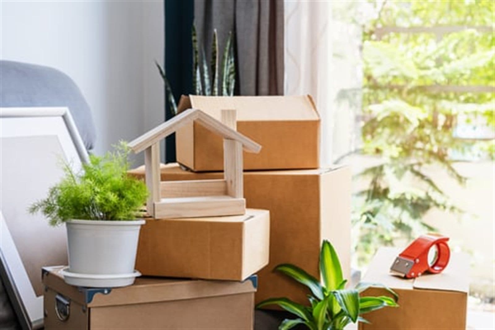 Moving boxes with a small wooden house model and a plant, representing a household relocation
