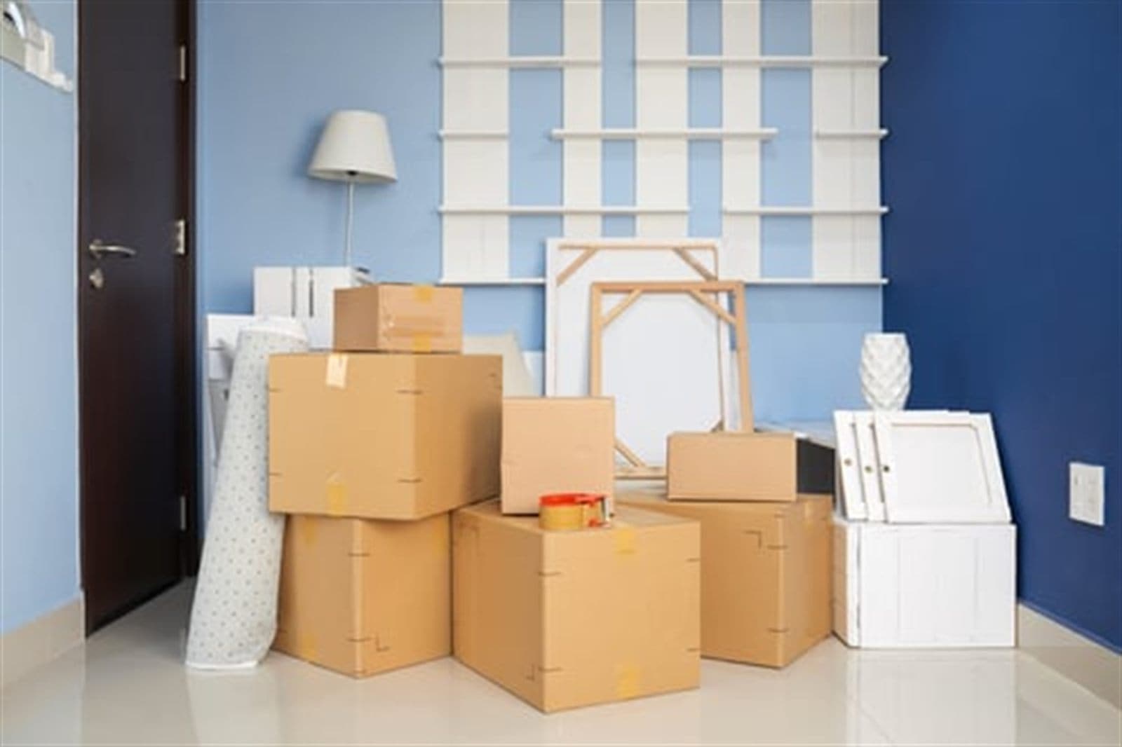 Moving boxes stacked against a blue accent wall in a home being packed for relocation